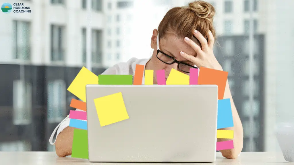 Woman is sitting behind open laptop. The laptop has many post-it notes stuck onto screen edge. Her head is resting on her left hand, conveying a feeling of overwhelm.