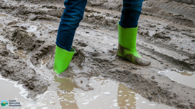 Picture shows very muddy and rutted ground with a pair of legs and wellies stuck in the mud.
